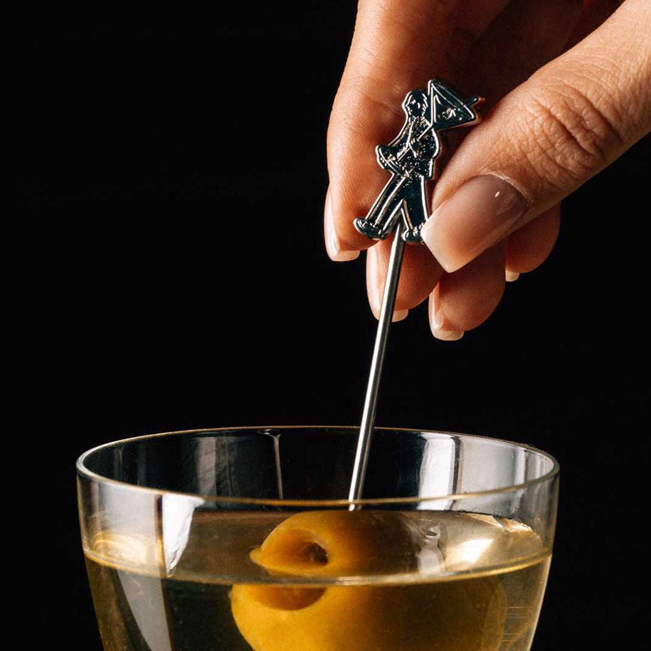 Hand using a Corner Store cocktail stirrer to stir a drink in a glass.
